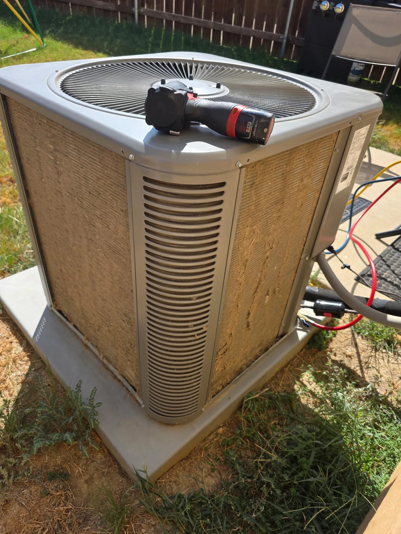 Outdoor AC condenser with its coil fins matted over by a thick layer of dust, lint and grass